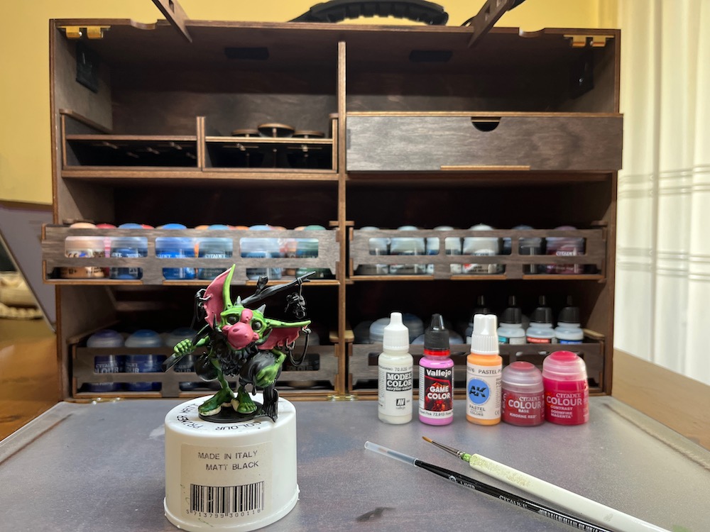 A goblin miniature standing in front of a portable painting workspace.